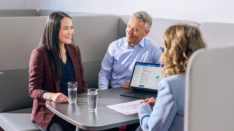 Three people in discussion at a table with laptop and documents