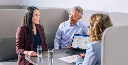 Three people in discussion at a table with laptop and documents