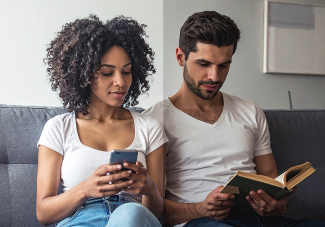 Two people sitting on a couch, one reading a book, the other using a smartphone