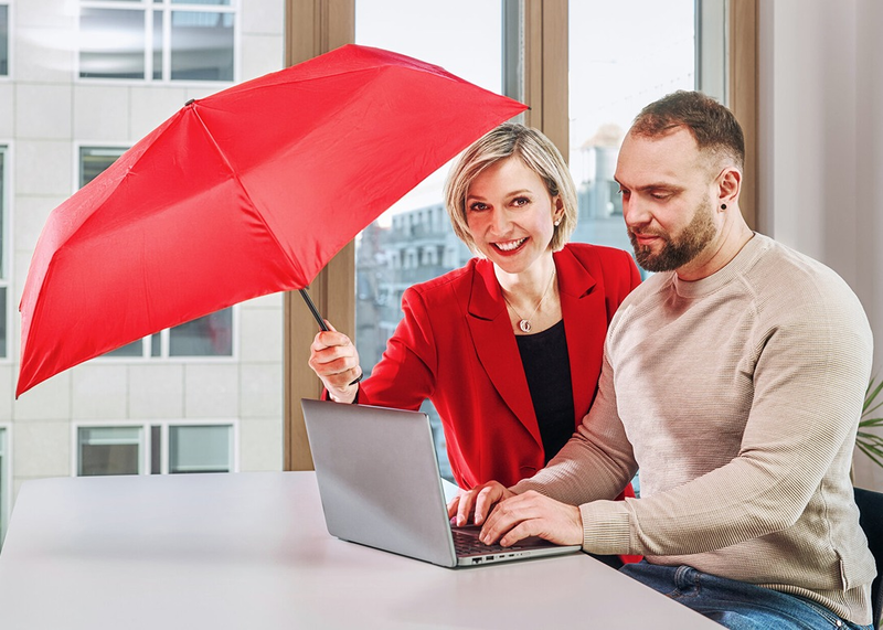 Two people collaborating on a laptop with a red umbrella symbolizing protection