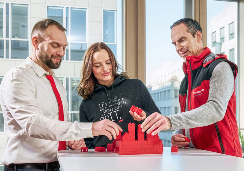 Three people building a tower with red blocks together