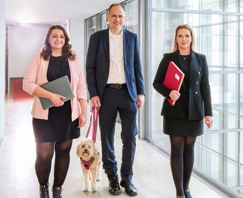 Three people walking through an office building with documents