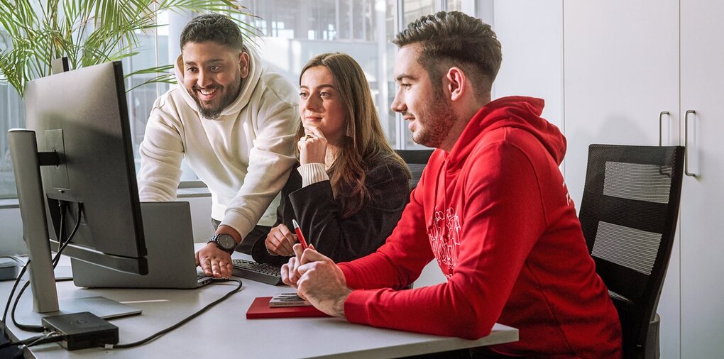 Three people in discussion with documents and laptop